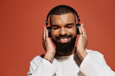 Şık görünüşlü genç adam kulaklık takarken gülümsüyor, müzik atmosferine dalmış..