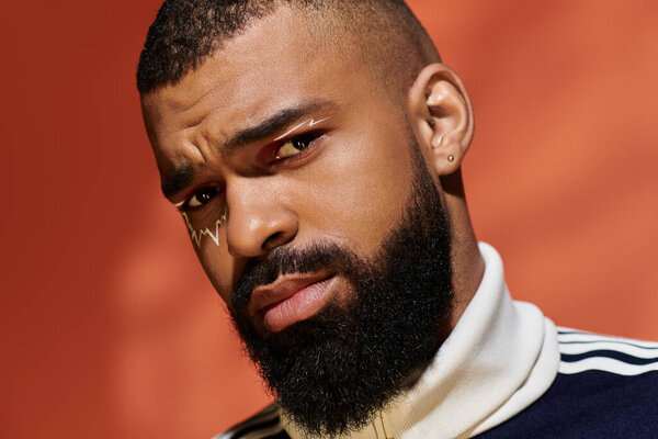 Стильный мужчина с ухоженной бородой уверенно позирует на ярком фоне.