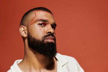 Genç, şık bir adam çarpıcı bir arka plana karşı cesur bir makyajla güven içinde poz verir..