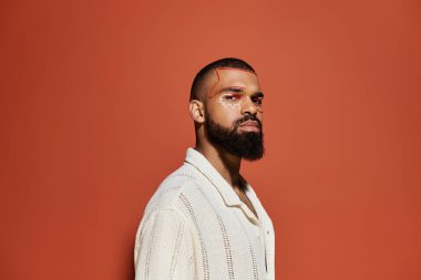 Çarpıcı bir yüz sanatı ile şık giyinmiş karizmatik bir genç adam, cesur bir arka plan tarafından çerçevelenmiş..