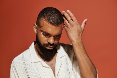 Yakışıklı genç adam turuncu bir arkaplana karşı şık bir elbise içinde poz veriyor, yaratıcı yüz sanatı sergiliyor..