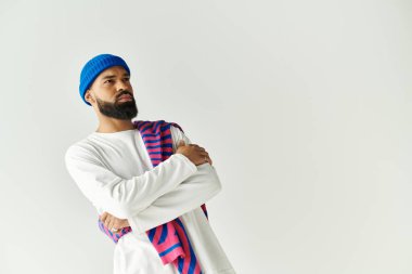 Sakallı, mavi bereli ve beyaz giysili yakışıklı bir adam kendine güvenen bir poz veriyor..