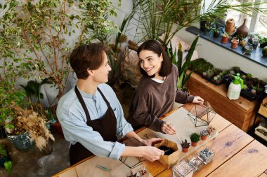 Yaratıcı çift, yeşilliklerle çevrili neşeli bir sanat stüdyosunda mutlu bir şekilde iş birliği yapıyor ve fikirleri paylaşıyor..