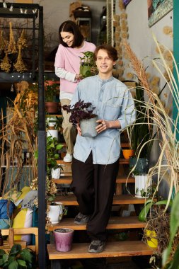 Genç çift, bitkiler ve yaratıcı malzemelerle çevrili canlı bir sanat stüdyosunun merdivenlerine tırmanıyor..