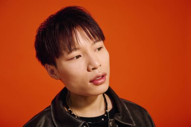 Kısa saçlı şık Asyalı adam parlak turuncu bir duvara karşı duruyor..