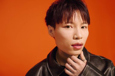 Yakışıklı bir Asyalı cesur bir turuncu arka plana karşı düşünceli bir şekilde poz verir..