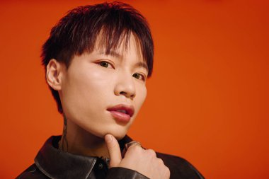 Havalı bir Asyalı, turuncu bir zemine karşı anlamlı bir poz verir..