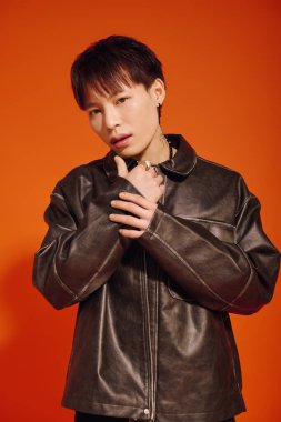 Kendine güvenen Asyalı genç adam, modern modayı deri ceketli ve çarpıcı aksesuarlarıyla sergiliyor.