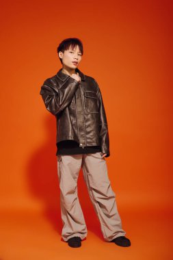 Genç yakışıklı adam şık deri ceketini ve rahat pantolonunu sergiliyor..