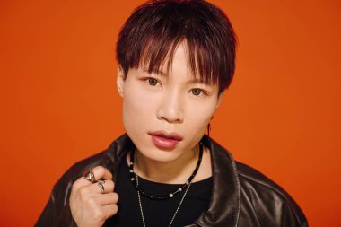 Şık, genç bir Asyalı, modasını turuncu bir arka planda sergiliyor..