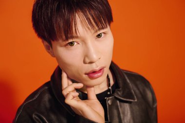 Genç, şık bir Asyalı cesur bir turuncu arka plana güvenerek poz veriyor..