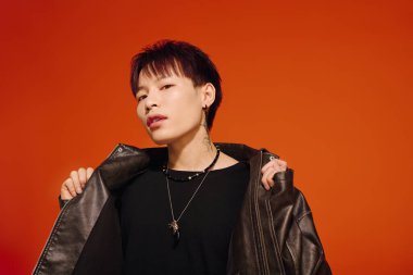 Şık ceketli genç bir Asyalı, turuncu bir fona karşı güven yayıyor..