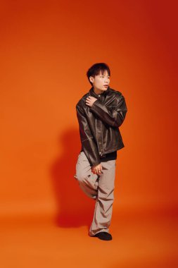 Siyah ceketli yakışıklı genç bir adam koyu turuncu bir duvara karşı açıkça poz veriyor..