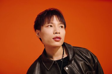 Moda kıyafetli genç adam cesur bir turuncu arka plana karşı özgüvenle poz veriyor..