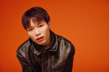 Yakışıklı bir Asyalı cesur bir turuncu zemine karşı stil ve güven yayıyor..