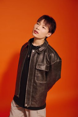 Yakışıklı Asyalı adam parlak turuncu bir arka planda kendine güvenerek poz veriyor. Moda yeteneği sergiliyor..