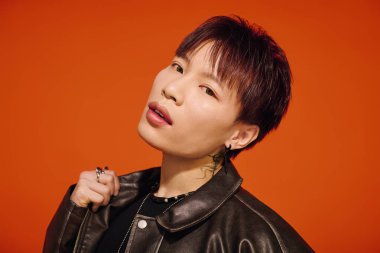 Deri ceketli şık bir genç adam canlı turuncu bir arka planda duruyor..