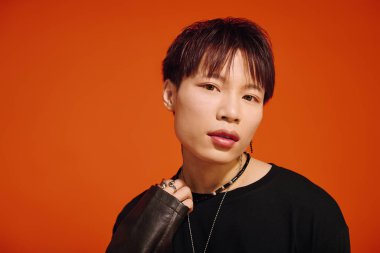 Şık giyinmiş yakışıklı genç adam, turuncu bir arka plana güvenerek poz veriyor..