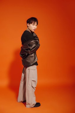 Şık bir genç adam cesur bir turuncu arka plana karşı özgüvenle duruyor..