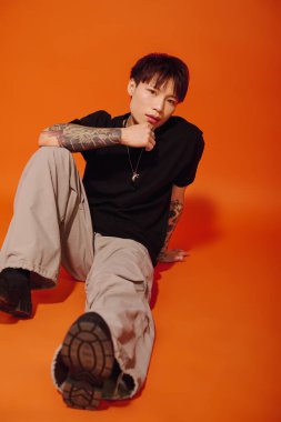 Şık, genç Asyalı bir adam yerde oturmuş, kendine has modasını sergiliyor..