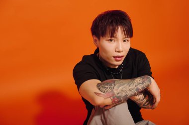 Yakışıklı genç adam tesadüfen oturuyor, benzersiz dövmeler ve şık kıyafetler sergiliyor..