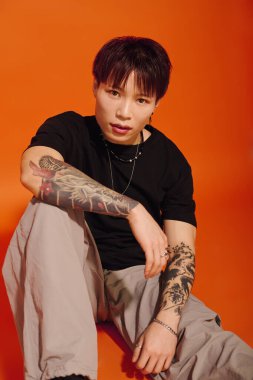 Dövmeleri olan kendine güvenen genç bir adam oturuyor ve eşsiz stilini ve kişiliğini sergiliyor..