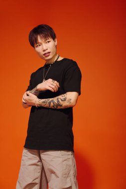 Yakışıklı genç bir adam şık kıyafetini ve dövmelerini kendine güvenen bir duruşta sergiliyor..