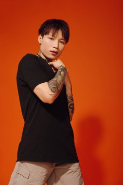 Zarif genç Asyalı adam canlı turuncu bir duvarın önünde güven içinde poz veriyor..