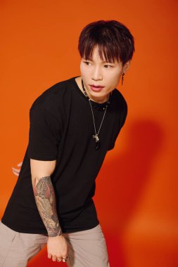 Şık bir Asyalı genç adam kendine güvenerek parlak turuncu bir duvara karşı modasını sergiliyor..