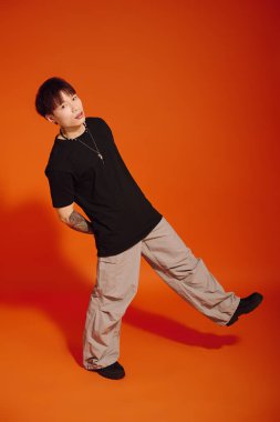 Kendine güvenen genç adam modern tarz ve karizma sergiliyor. Parlak bir ortamda neşeli bir duruşu var..