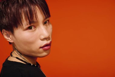 Genç, yakışıklı Asyalı bir adam parlak turuncu bir arka planda şık kıyafetini modelliyor..