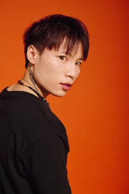 Genç, modaya uygun Asyalı bir adam kendine güvenen bir ifadeyle arkasına bakar, şık görünümünü gösterir..