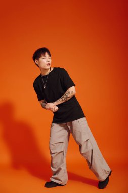 Yakışıklı Asyalı genç bir adam siyah gömleği ve açık renk pantolonu içinde zarif bir şekilde duruyor..