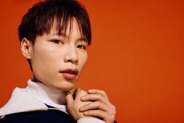 Yakışıklı bir Asyalı genç adam moda anlayışını, kalın turuncu bir duvara karşı sergiliyor..