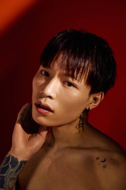 Çarpıcı dövmeleri olan şık bir Asyalı genç adam sanatsal bir ortama yoğun bir şekilde bakıyor..