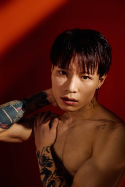 Sıcak ışıkta kendine güvenen bir duruş sergilerken dövmelerini gösteren şık genç bir adam.