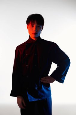 Yakışıklı genç bir adam kendine güvenerek ayakta duruyor, şık kıyafetini parlak bir arkaplanda sergiliyor..