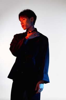 Kendine güvenen Asyalı adam dinamik ışıklandırmalı şık bir kıyafet içinde düşünceli bir şekilde poz veriyor..