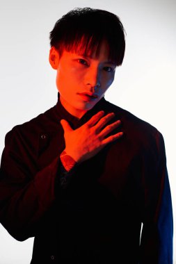 Yakışıklı Asyalı adam şık giyinmiş dramatik ışıklandırmayla kendine güvenli bir poz veriyor..