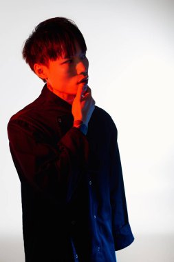 Şık bir Asyalı adam düşünceli bir şekilde ayakta duruyor, elleri çenesinde, kendine güveni tam..