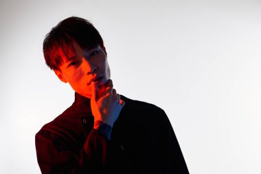 Zarif genç bir Asyalı stüdyoda büyüleyici bir şekilde poz veriyor, entrika ve güven yayıyor..