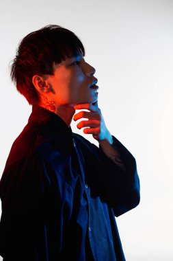 Yakışıklı bir Asyalı genç adam, yaratıcı ve renkli bir ortamda kendini kaybederken çenesine dokunur..