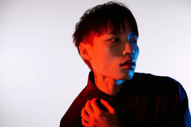 Genç bir adam şık görünümünü, çarpıcı renkli ışıklarla aydınlatılmış cesur bir pozla sergiliyor..