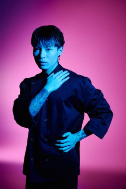 Şık giyinmiş, dövmeli, kendine güveni tam Asyalı bir adam renkli bir poz veriyor..