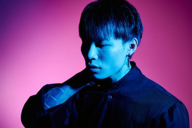 Şık bir Asyalı genç adam canlı ve sanatsal bir arkaplana karşı düşünceli bir şekilde poz verir..