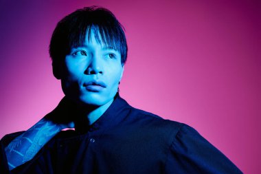 Yakışıklı bir Asyalı şık bir görünüm sergiliyor. Renkli bir atmosferde kendine güvenen bir duruş sergiliyor..