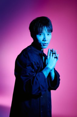 Şık bir Asyalı genç adam ellerini sanatsal ışıklandırmaya sıkıştırarak poz veriyor..