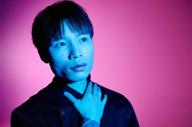 Genç, yakışıklı Asyalı bir adam canlı ve renkli bir geçmişe karşı zarif bir şekilde duruyor..