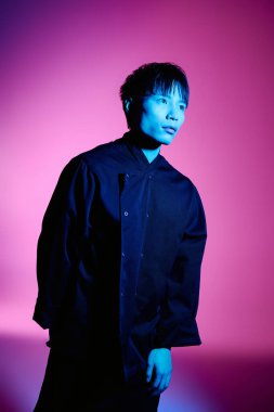 Yakışıklı Asyalı adam, çarpıcı sanatsal bir mekanda, cesur renklerle aydınlatılmış, özgüvenle duruyor..