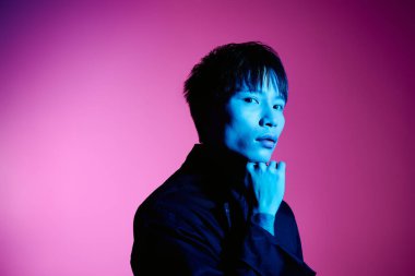 Genç, şık Asyalı bir adam canlı mor bir arka plana karşı zarif bir şekilde poz verir..